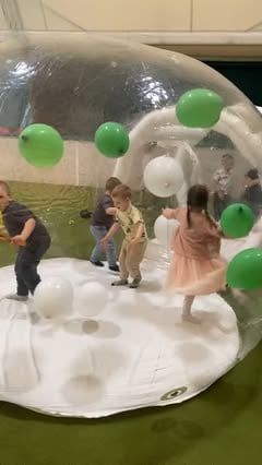 Deca se igraju unutar prozirne kupole na naduvavanje sa zelenim i belim balonima